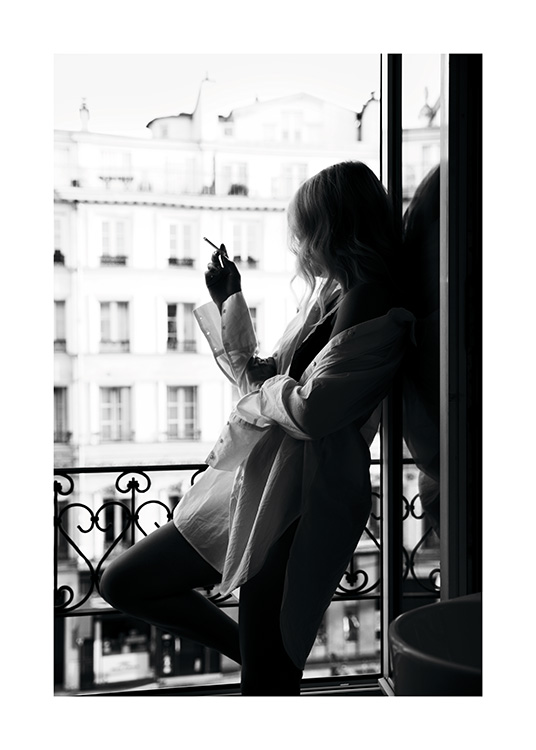  – Black and white photograph of a woman in an oversized shirt smoking a cigarette in a window