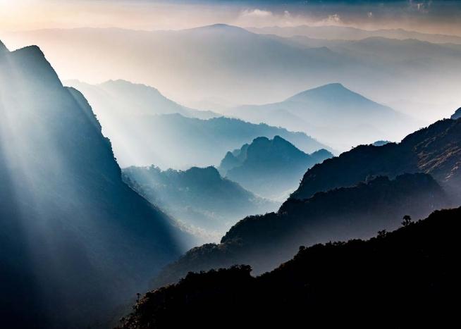 – Photograph of foggy mountains with the sun shining through. 