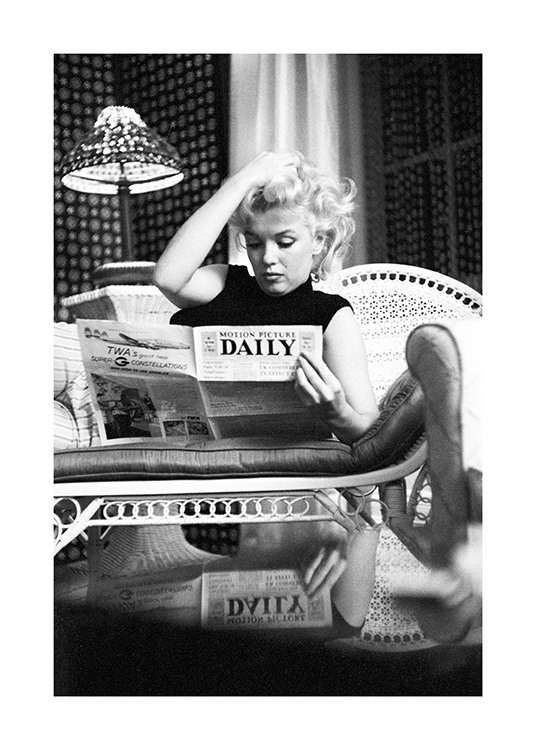  – Black and white photograph of the icon Marilyn Monroe while she's reading a newspaper on the sofa