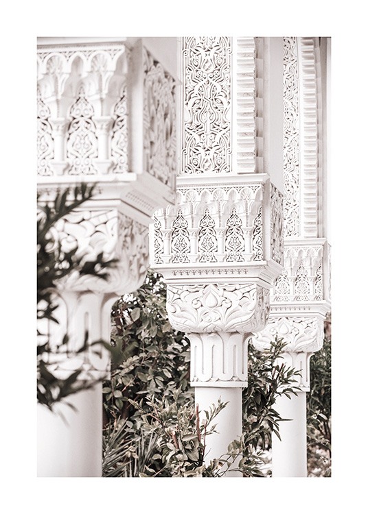  - Photograph of crafted white pillars with patterns and green leaves in the background