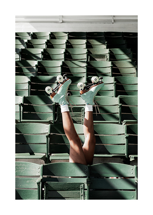  – Photograph of a person wearing roller skates stretching their legs up between green seats at a stadium