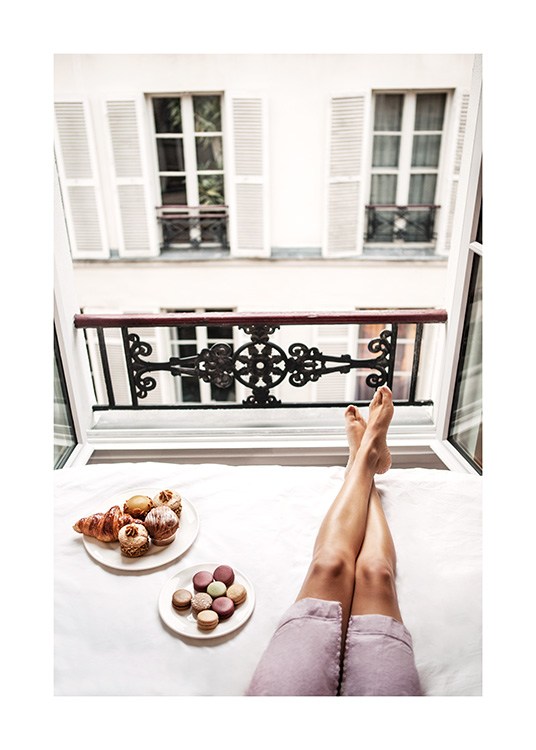  – Photograph of plates with buns and macarons next to a pair of legs in a window