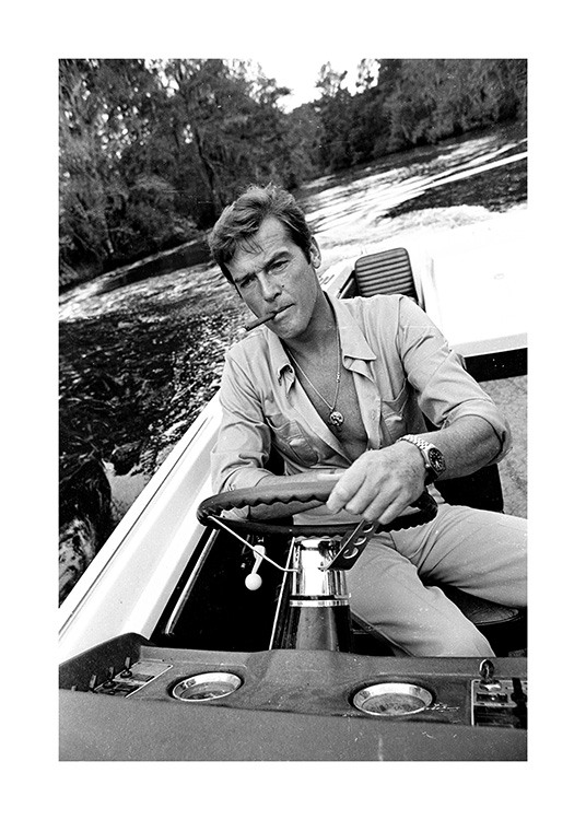  – Black and white photograph of Roger Moore driving a boat with a cigarette in his mouth