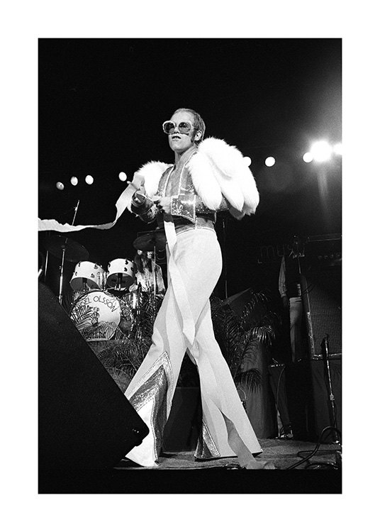 – Black and white photograph of the singer Elton John, wearing a white jumpsuit and sunglasses on stage