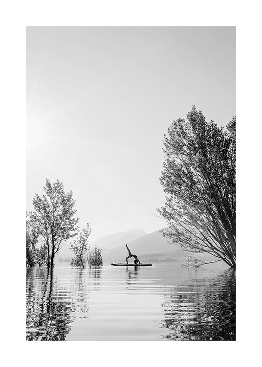  – Black and white photograph of a woman in a yoga pose on a surfboard in the middle of a lake