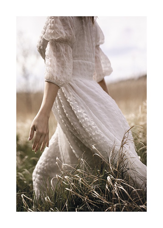  – Photograph of a woman in a dress in white, walking through a grass field