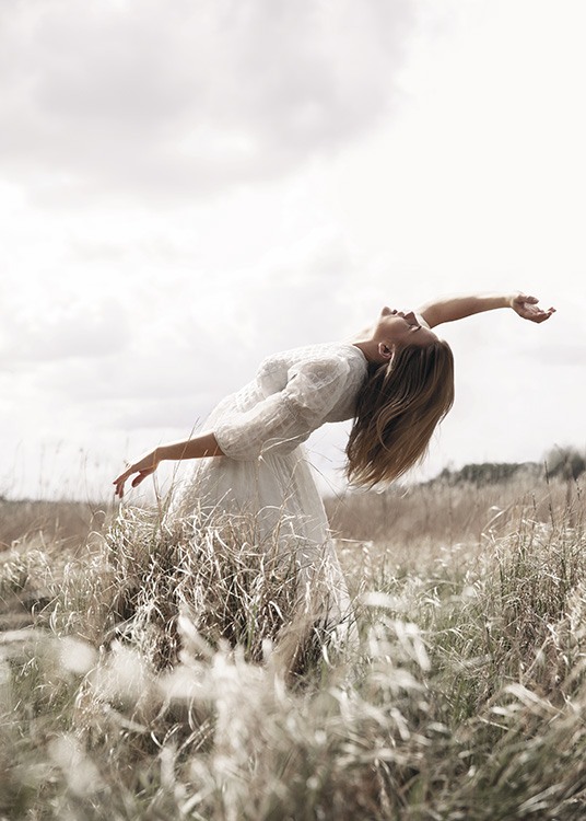  – Photograph of a woman posing in a field with grass, wearing a white dress