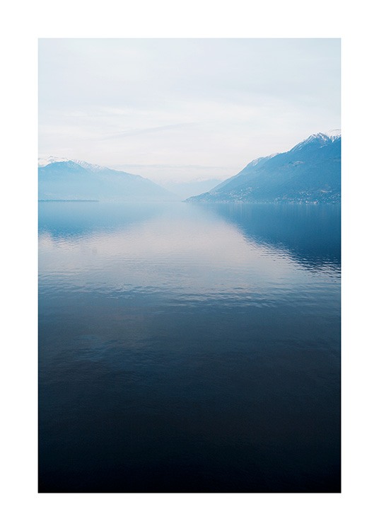  – Photograph of a lake with a still surface, with mountains and fog in the background