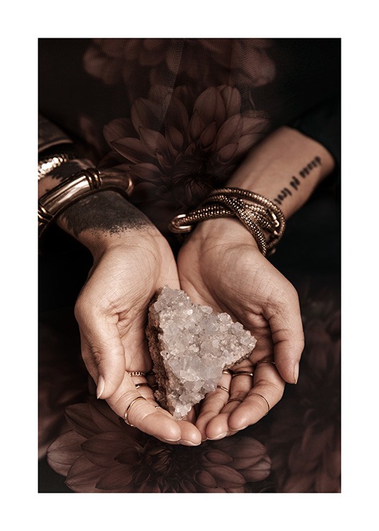  – Photograph of a crystal in cupped hands, with dark flowers in the background