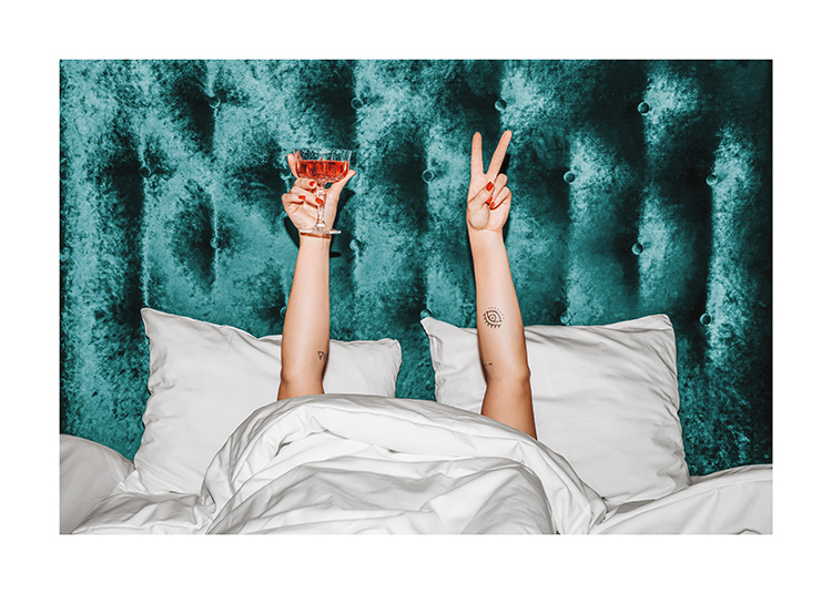  – A woman holding an orange drink in a bed with a turquoise velvet headboard