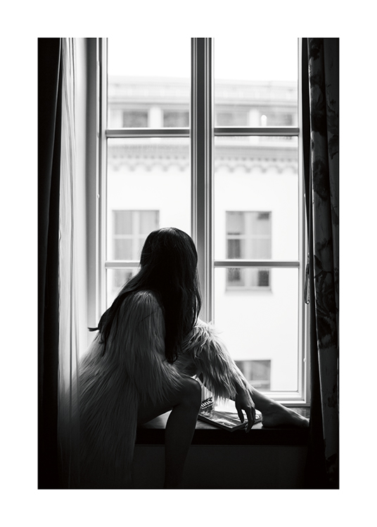  – A black and white photo of a dark-haired woman sitting on a windowsill in a faux-fur jacket