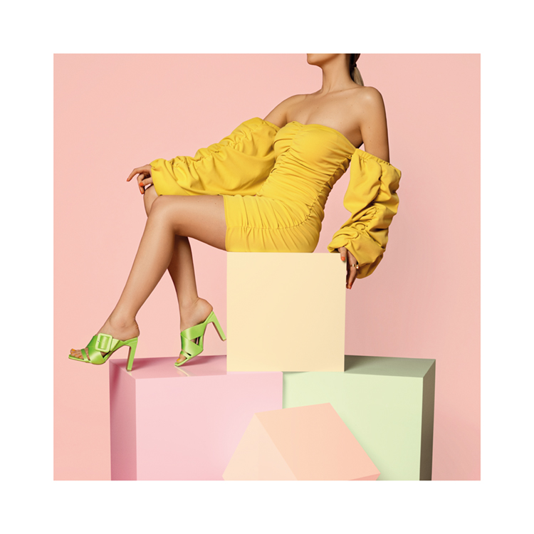  – A woman sitting on the top of colored boxes in a yellow dress and green heels
