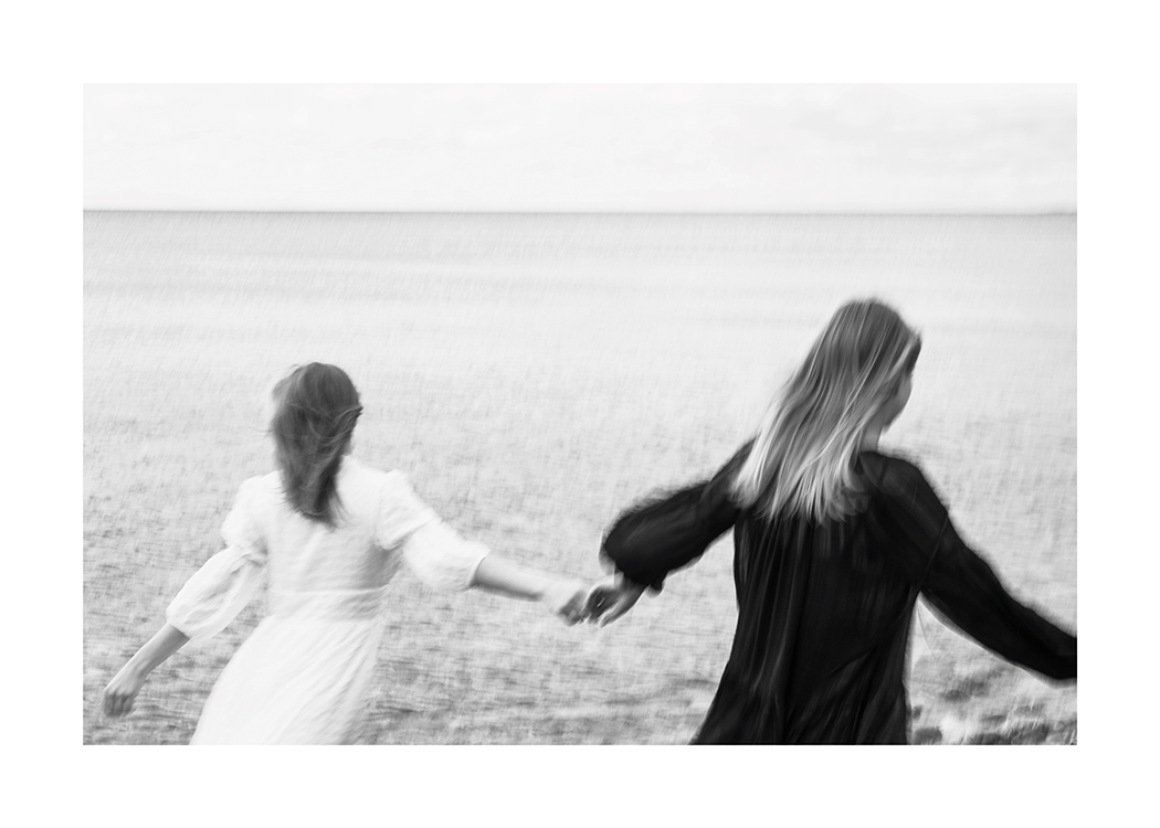  – Black and white photograph of a pair of women running across a field whilst holding each others hands