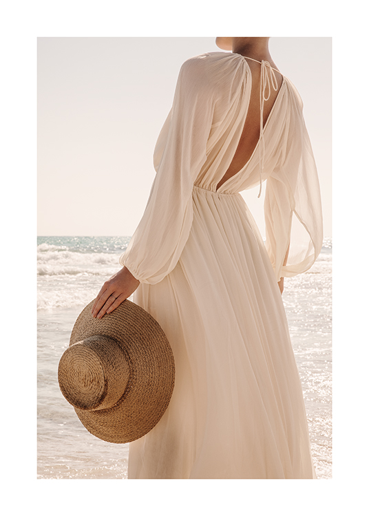  – A woman on the beach holding a hat, standing in the sunlight