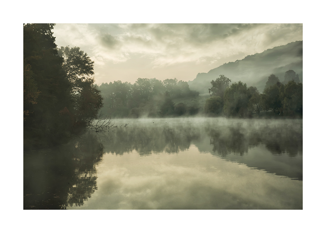  – Photograph of a still lake with fog over the water and a forest in the background